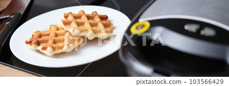 Delicious fresh sweet cooking waffles on plate in kitchen Delicious fresh sweet cooking waffles on plate in kitchen 103566429