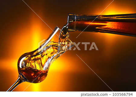 Pouring alcohol into a glass on dark background 103566794