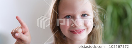 Portrait of cheerful smiling child girl points finger to side 103567372