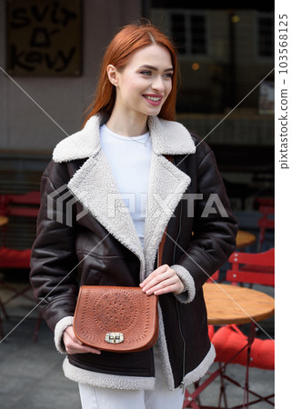 a red-haired girl in a leather jacket. cheerful woman with long red hair poses for a photographer a red-haired girl in a leather jacket. cheerful woman with long red hair poses for a photographer 103568125