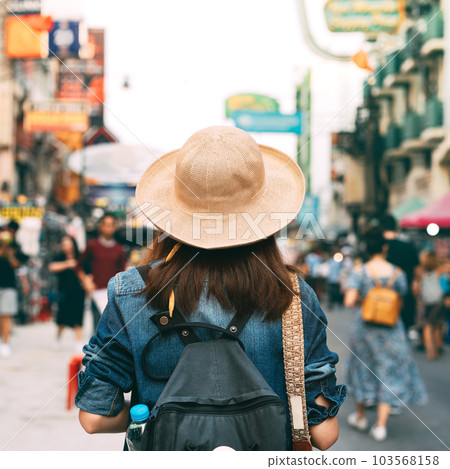 Rear view of backpack adult traveller woman wearing denim shirt and hat at outdoor street market 103568158