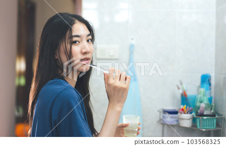 Young adult asian woman brushing teeth in font of bathroom mirror. Young adult asian woman brushing teeth in font of bathroom mirror. 103568325