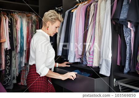 Mature woman chooses or organizes clothes and things in drawer in wardrobe closet dressing room at home 103569850