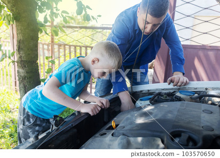 Timing belt break. Man and son near hood of car is looking for a malfunction due to which the engine does not work. Driver is holding a broken front belt in his hands. Shock due to irreparable damage. 103570650