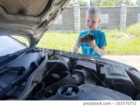 A mechanic dad teaches his son how to change the timing belt and car cooling pump at home. Child holds a pump in his hand. Maintenance of the car according to the regulations. New parts A mechanic dad teaches his son how to change the timing belt and car cooling pump at home. Child holds a pump in his hand. Maintenance of the car according to the regulations. New parts 103570751