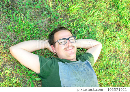 Young man with glasses lied on grass enjoying vacation after studying very happy 103571921