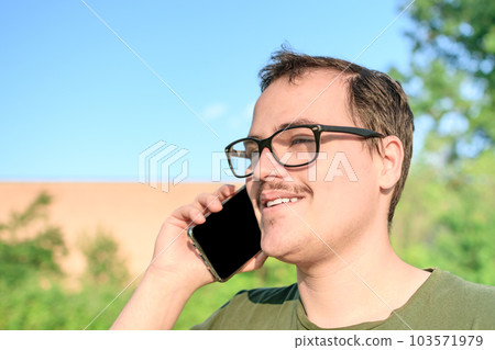 Young man with eyeglasses and green t-shirt talking on cell phone at the park Young man with eyeglasses and green t-shirt talking on cell phone at the park 103571979