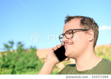 Young man with eyeglasses and green t-shirt talking on cell phone at the park 103571994