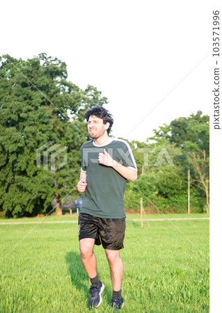 Young man with green t-shirt exercising and with gesture of suffering in park 103571996