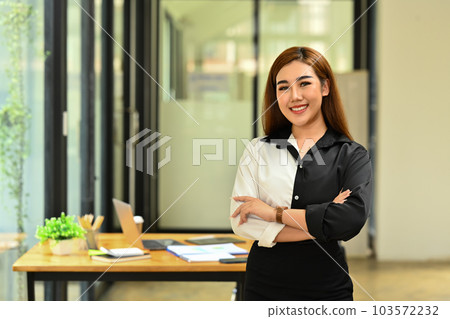 Confident millennial businesswoman wearing stylish clothes standing with crossed arms and smiling to camera Confident millennial businesswoman wearing stylish clothes standing with crossed arms and smiling to camera 103572232