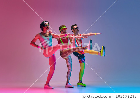 Three men in vintage, funny, colorful sportswear training, stretching against gradient blue pink studio background. Aerobics Three men in vintage, funny, colorful sportswear training, stretching against gradient blue pink studio background. Aerobics 103572283