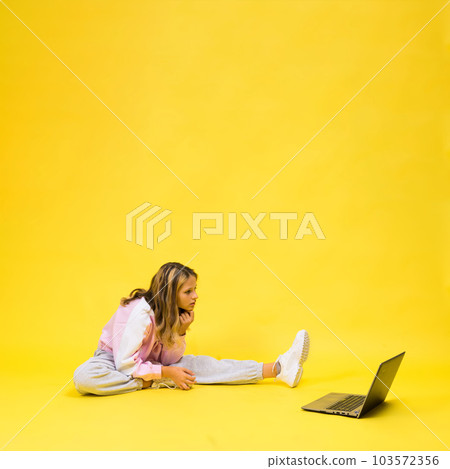 Positive kid sit with laptop read homework wear casual style cloth isolated over yellow background Positive kid sit with laptop read homework wear casual style cloth isolated over yellow background 103572356