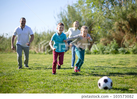 Father with mother with two children enjoy playing soccer on lawn in summer park Father with mother with two children enjoy playing soccer on lawn in summer park 103573082