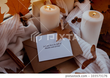 LET OUR LIVES BE FULL OF THANKS AND GIVING text greeting card concept Celebrating autumn holidays at cozy home on the windowsill Hygge aesthetic atmosphere Autumn leaves spices and candle on knitted 103573176