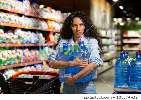 A young woman buys pallets of water in a supermarket. He takes it in his hands, packs it in a cart. Panic during a pandemic, quarantine 103574432