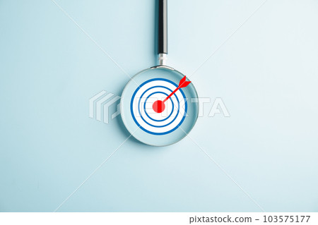 A magnifier glass focuses on a target board, highlighting the significance of business objectives. Against a background, it symbolizes the concepts of search, goal attainment, and strategic planning. A magnifier glass focuses on a target board, highlighting the significance of business objectives. Against a background, it symbolizes the concepts of search, goal attainment, and strategic planning. 103575177