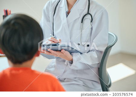 A young female doctor interviewing an elementary school boy 103576574