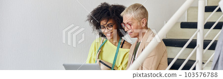 Mature woman and young African-American use laptop stitting on staircase in design studio 103576788