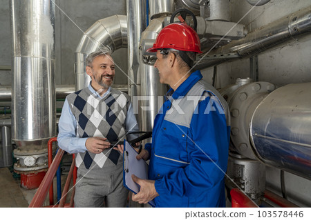 Smiling Manager and Worker in Red Hardhat and Blue Uniform Having Conversation in Industrial Interior 103578446