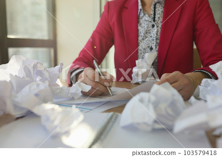 Woman writes reports at table covered with crumpled papers Woman writes reports at table covered with crumpled papers 103579418