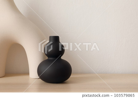Set of modern ceramic vases of geometric organic shape on wooden table. Modern black sculpture. Beige wall. Abstract trendy artistic background, web banner. 103579865
