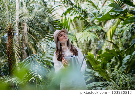 Portrait of young gardener taking care of plants in her greenhouse. 103580813