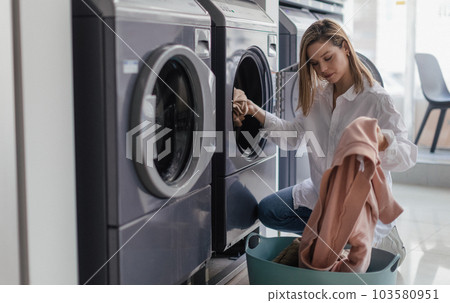 Young woman loading washing machine in public laundry. 103580951