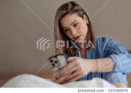Young woman lying on a bed and scrolling her smartphone. Young woman lying on a bed and scrolling her smartphone. 103580976
