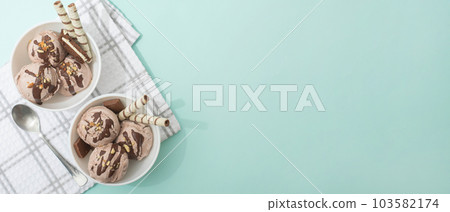 Chocolate homemade ice cream decorated with nuts, chocolate chips, wafer rolls, in white bowl. Summer cooling desserts Chocolate homemade ice cream decorated with nuts, chocolate chips, wafer rolls, in white bowl. Summer cooling desserts 103582174