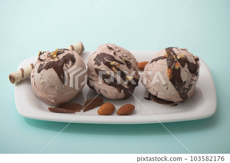 Chocolate ice cream in balls decorated with nuts and chocolate icing, blue background. Summer cooling desserts, cafe menu Chocolate ice cream in balls decorated with nuts and chocolate icing, blue background. Summer cooling desserts, cafe menu 103582176