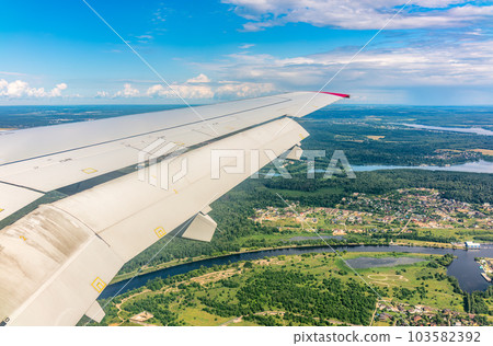 View of airplane wing, blue skies and green land during landing. Airplane window view. 103582392