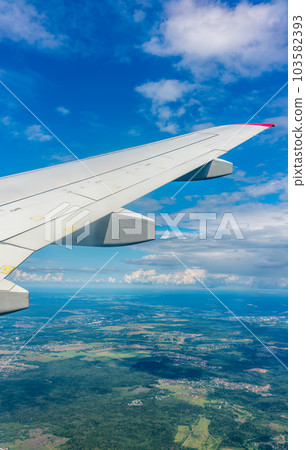 View of airplane wing, blue skies and green land during landing. Airplane window view. View of airplane wing, blue skies and green land during landing. Airplane window view. 103582393