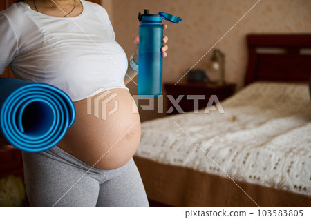 Close-up bare belly with stretch marks of a pregnant woman in gray leggins and white crop t-shirt, carrying a blue exercise mat and bottle with water. Pregnancy yoga and fitness. Childbirth. Maternity Close-up bare belly with stretch marks of a pregnant woman in gray leggins and white crop t-shirt, carrying a blue exercise mat and bottle with water. Pregnancy yoga and fitness. Childbirth. Maternity 103583805