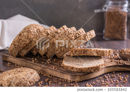 Sliced buckwheat bread on a cutting board and cereals on the table Sliced buckwheat bread on a cutting board and cereals on the table 103583842