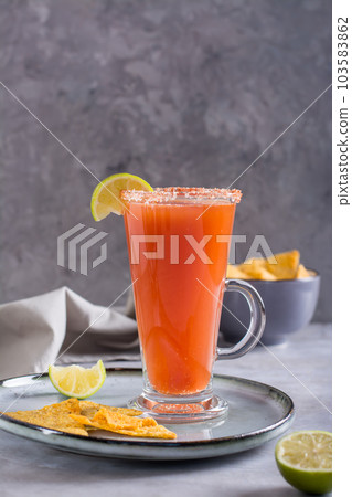 Michelada cocktail with tomato juice, beer and lime in a glass and nachos vertical view Michelada cocktail with tomato juice, beer and lime in a glass and nachos vertical view 103583862