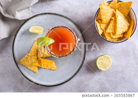 Michelada cocktail with tomato juice, beer and lime in a glass and nachos top view Michelada cocktail with tomato juice, beer and lime in a glass and nachos top view 103583867