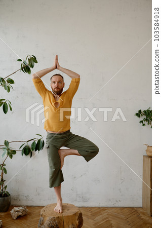 Strong yogi man balancing on wooden stump in tree yoga pose Vrikshasana 103584918