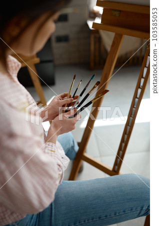 Young woman artist choosing paintbrush preparing to draw picture Young woman artist choosing paintbrush preparing to draw picture 103585053