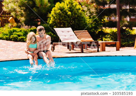 Dad and daughter have fun and and sit on the edge of the pool  103585193