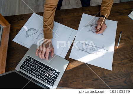 Unrecognizable male architect sketching construction project with laptop drawings drawing blueprint 103585379