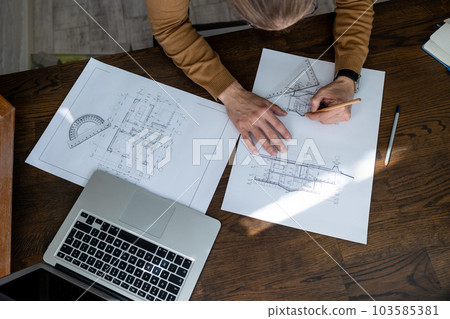 Unrecognizable male architect sketching construction project with laptop drawings drawing blueprint 103585381