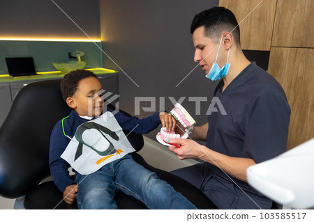 Doctor showing jaw mock-up to dark-skinned kid Doctor showing jaw mock-up to dark-skinned kid 103585517