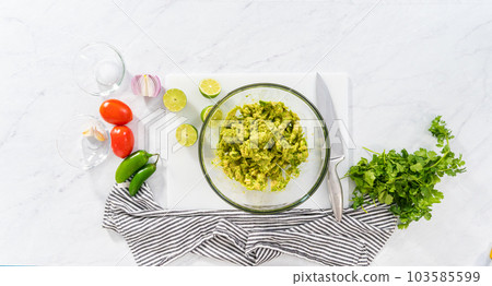 Flat lay. Mixing ingredients in a glass mixing bowl to prepare classic guacamole dip on the counter. Flat lay. Mixing ingredients in a glass mixing bowl to prepare classic guacamole dip on the counter. 103585599