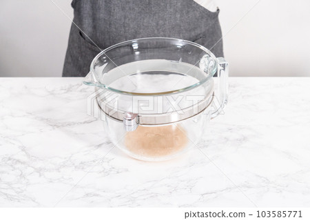 Activating dry yeast in a large glass mixing bowl to prepare the pizza dough. 103585771