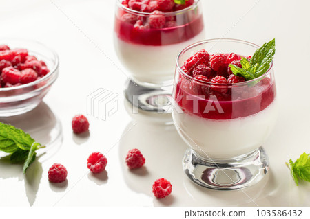 Panna cotta with raspberry jelly and mint leaves in glass glasses on a white table 103586432