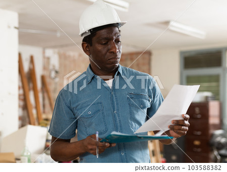 Strict building inspector standing with papers at construction site 103588382