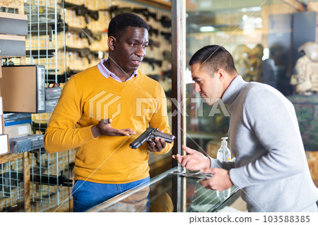 Seller consulting buyer about pistol in arms shop 103588385