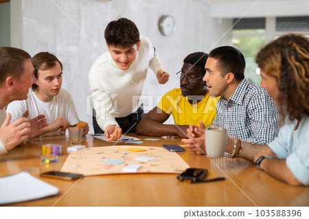 Group of enthusiastic men playing board game sitting around table 103588396