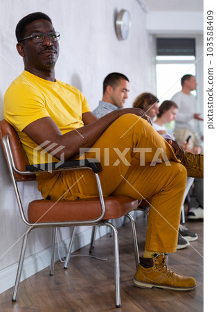 Middle-aged male visitor sitting on chair in waiting hall of clinic Middle-aged male visitor sitting on chair in waiting hall of clinic 103588409