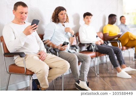 Middle-aged male visitor sitting on chair in waiting hall of clinic 103588449